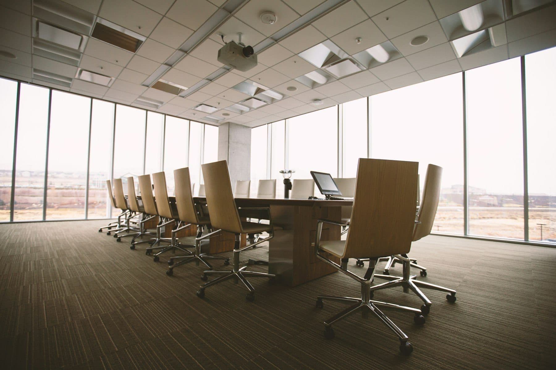 A long wooden conference table in warm light, chairs squared and waiting
